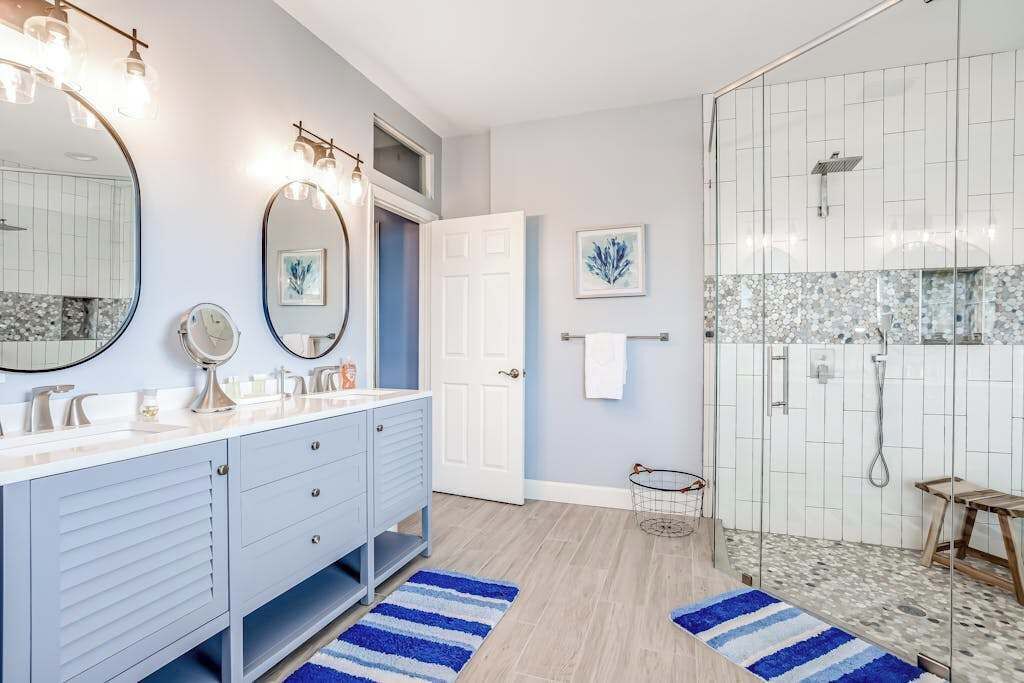 A bathroom with a vanity, two mirrors, a shower, and a door.