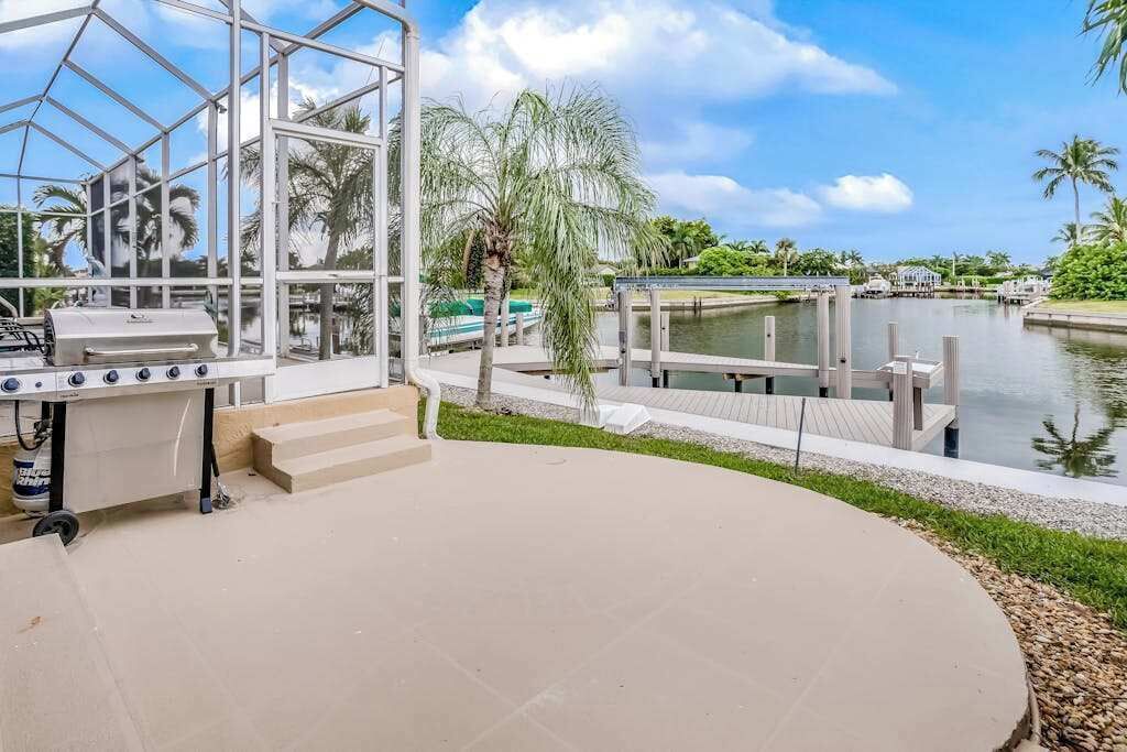A patio area with a grill, a glass enclosure, and a water body with docks.