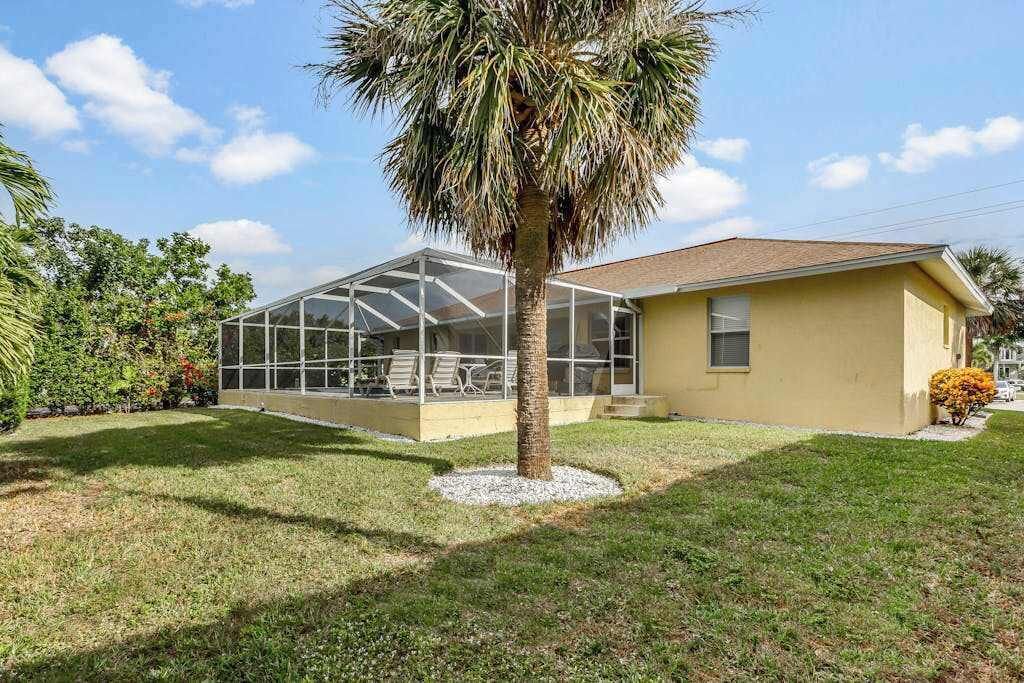 A single-story house with a glass-enclosed porch, a palm tree, and a well-maintained lawn.