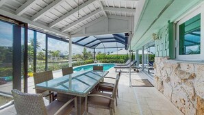 Eine Terrasse im Freien mit einem Glastisch, Korbstühlen, einem Swimmingpool und einer Steinmauer.