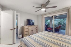 A bedroom with a bed, a TV on a dresser, a ceiling fan, and a sliding glass door leading to an outdoor area with a chair. - Dog-friendly single-level condo with furnished patio, rooftop, & washer/dryer (Naples)