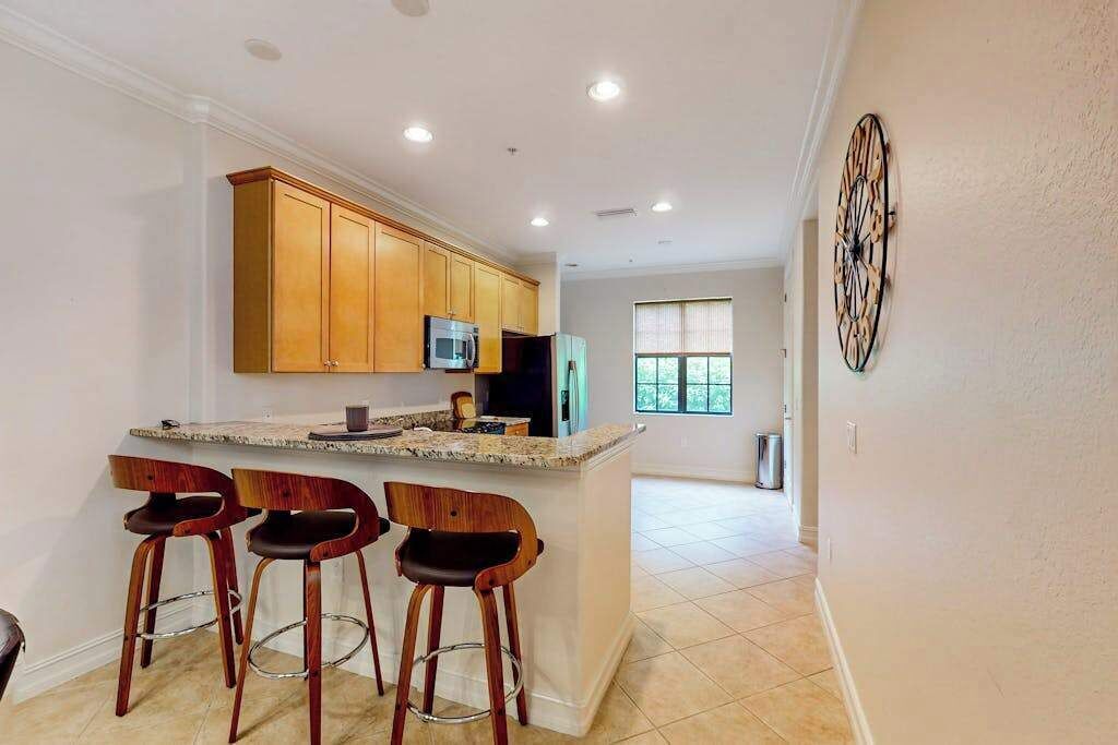 A kitchen with wooden cabinets, a microwave, and a bar area with stools.