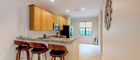 A kitchen with wooden cabinets, a microwave, and a bar area with stools.