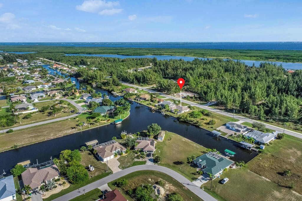 Luftaufnahme einer Wohngegend mit Häusern und einem Fluss, sowie einem roten Markierungspunkt.