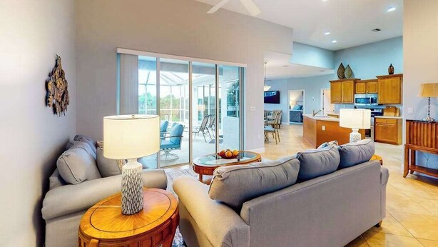 Una sala de estar moderna con sofá, mesa de centro y lámpara. Cuenta con una zona de cocina con armarios y televisión.