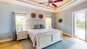 Un dormitorio con cama, mesitas de noche, ventilador de techo y un ventanal grande.