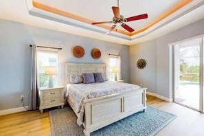 A bedroom with a bed, bedside tables, a ceiling fan, and a large window. - Spacious home with private pool, spa, patio, grill, AC, & W/D (Port Charlotte)
