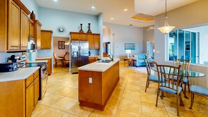 Una cocina amplia con armarios de madera, una isla central y un comedor con mesa y sillas de vidrio.