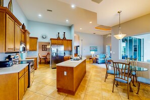 A spacious kitchen with wooden cabinets, a central island, and a dining area with a glass table and chairs. - Spacious home with private pool, spa, patio, grill, AC, & W/D (Port Charlotte)