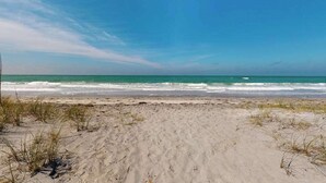 En strand med sand og lidt græs, der møder havet.