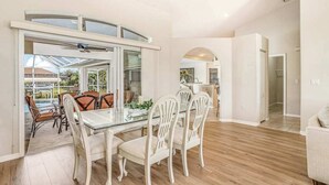 A dining area with a glass table and white chairs, a kitchen in the background, and a view of a swimming pool. - Dog-friendly home with private heated pool, grill, A/C, & washer/dryer (Port Charlotte)