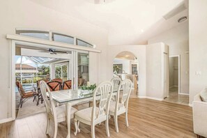 A dining area with a glass table and white chairs, a kitchen in the background, and a view of a swimming pool. - Dog-friendly home with private heated pool, grill, A/C, & washer/dryer (Port Charlotte)