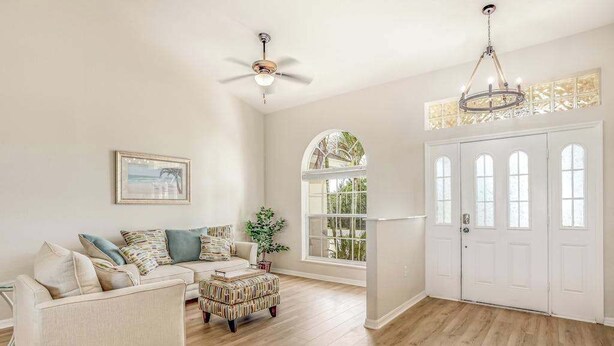 A living room with a sofa, ottoman, ceiling fan, and a large window. - Dog-friendly home with private heated pool, grill, A/C, & washer/dryer (Port Charlotte)