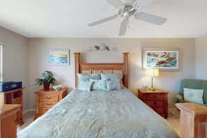 A bedroom with a bed, a ceiling fan, two bedside tables, a nightstand, a chair, and two wall-mounted paintings. - Snowbird-friendly condo with pool access, lake views, W/D, and central AC (Naples)