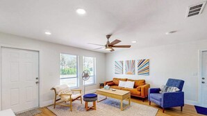 A living room with a ceiling fan, a wooden coffee table, a blue armchair, and a sofa with orange cushions. - Charming coastal getaway with lanai, bikes - near incredible beaches & golf (Naples)