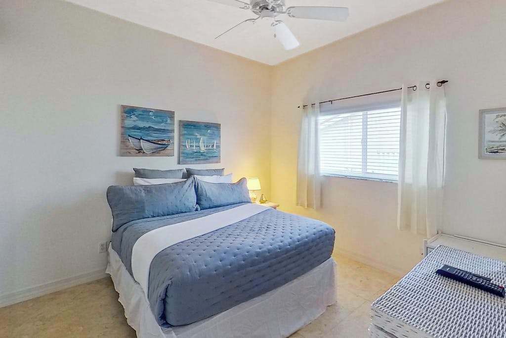 Une chambre à coucher avec un lit, un ventilateur de plafond, une fenêtre avec des rideaux et des œuvres d’art accrochées au mur.