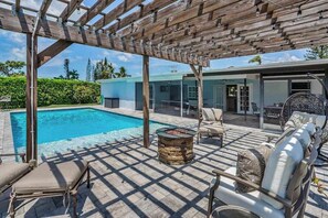 A poolside area with a pergola, outdoor seating, and a stone fire pit. - Inviting retreat with a large yard, heated pool, firepit, games & modern charm (Naples)