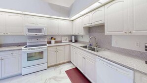 Una cocina moderna con armarios blancos, horno empotrado, microondas, lavavajillas y encimera de granito.