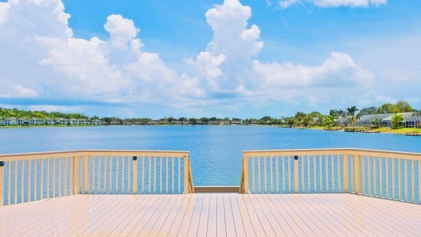 Un muelle de madera con vista a un lago tranquilo y edificios lejanos.