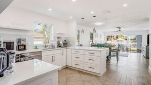 A modern kitchen with white cabinetry, a large island, and a dining area with a view. - Dog-friendly home plus attached studio with fenced yard, washer/dryers, & AC (Naples)
