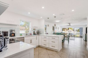 A modern kitchen with white cabinetry, a large island, and a dining area with a view. - Dog-friendly home plus attached studio with fenced yard, washer/dryers, & AC (Naples)