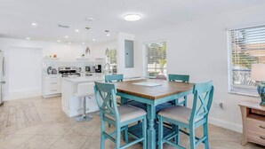 A modern kitchen with white cabinetry, a central island, and a dining area with blue chairs. - Dog-friendly home plus attached studio with fenced yard, washer/dryers, & AC (Naples)