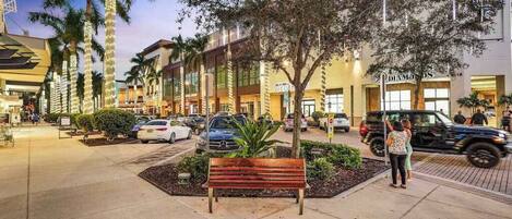 A shopping area with benches, palm trees, and a variety of storefronts.