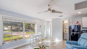 A spacious living room with a ceiling fan, a dining area with chairs, a kitchen with a refrigerator, and a view through large windows. - Dog-friendly home plus attached studio with fenced yard, washer/dryers, & AC (Naples)