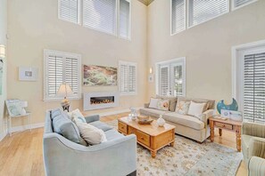 A spacious living room with a fireplace, two sofas, a coffee table, and large windows with shutters. - Waterfront home with private pool, dock, patio, balconies, & bikes (Matlacha)