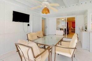 A room with a glass-top table, six chairs, a ceiling fan, and a flat-screen TV mounted on the wall. - Bright Florida home with pool, gas grill, private pool, and washer/dryer (Rotonda West)