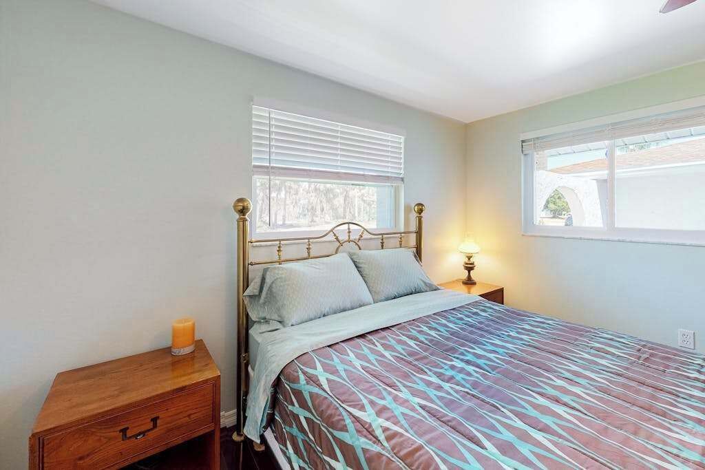 A bedroom with a bed, nightstand, and window with blinds.