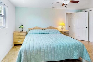 A bedroom with a bed, a nightstand, a lamp, a ceiling fan, and a door. - Bright Florida home with pool, gas grill, private pool, and washer/dryer (Rotonda West)
