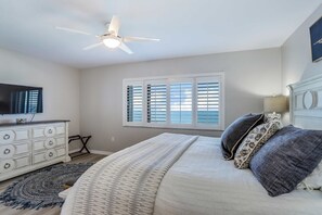 A bedroom with a bed, a dresser, a ceiling fan, a window with blinds, and a TV on the wall.
