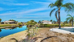 A residential area with houses, a small pond, and a palm tree. - Palm-lined waterfront retreat with enclosed pool, inviting patio, & central AC (Rotonda West)