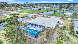 A residential area with a house featuring a large glass-enclosed pool, surrounded by a well-maintained lawn and palm trees. - Palm-lined waterfront retreat with enclosed pool, inviting patio, & central AC (Rotonda West)