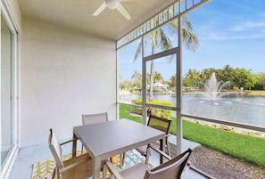 Ein Balkon mit Tisch und Stühlen, mit Blick auf einen Teich und Palmen.