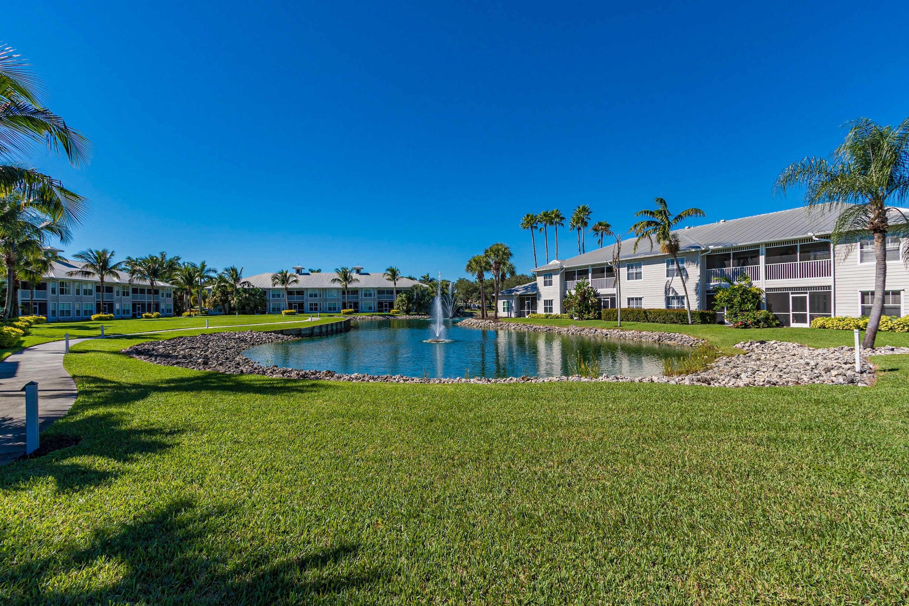 A hotel with a swimming pool, palm trees, and a clear blue sky.