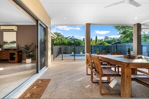 A spacious patio with a wooden table and chairs, a pool, and a view of greenery. - Zen Lotus Private Pool - Patio - Garage - Yard (Darwin)