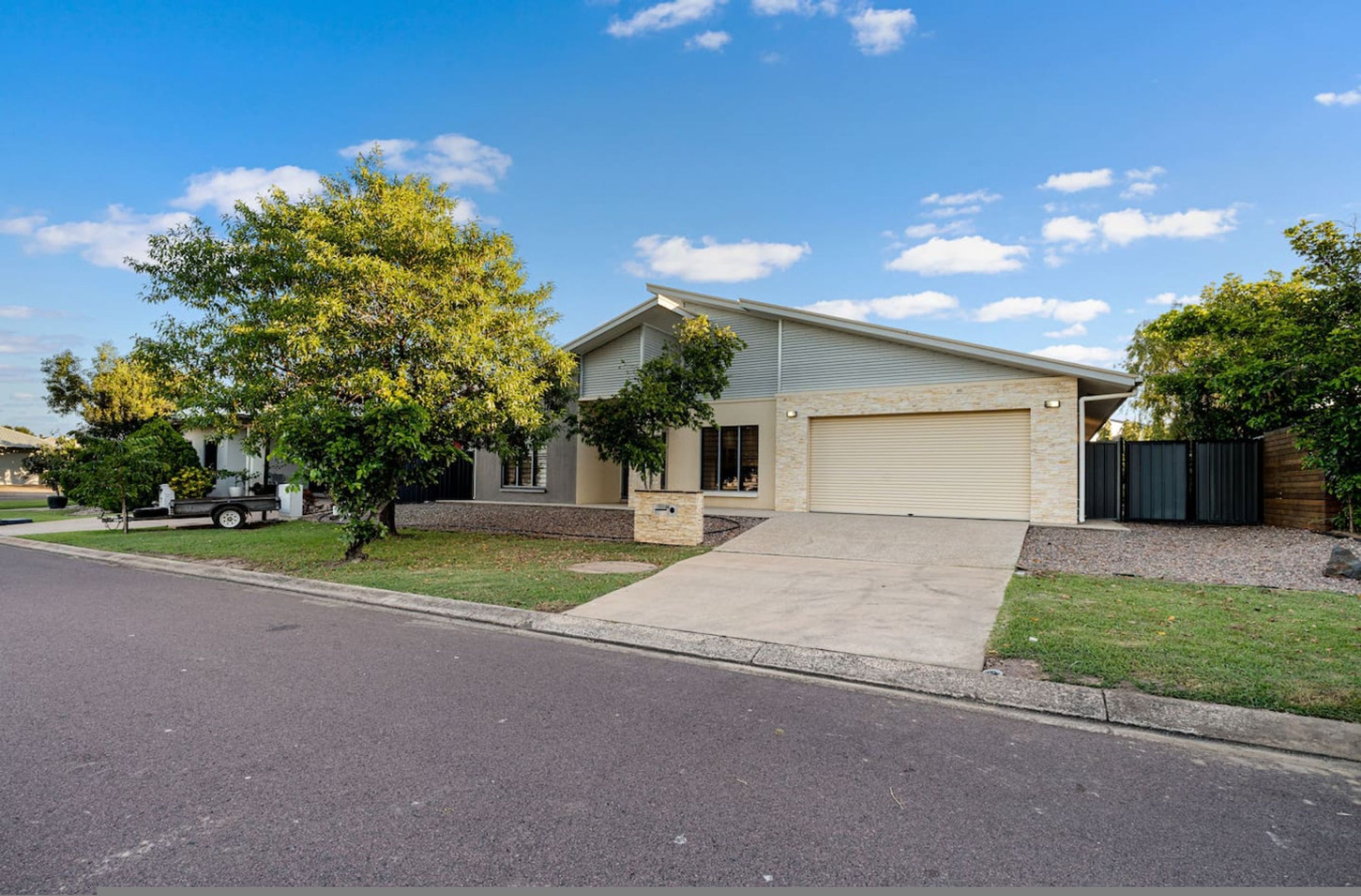 A single-story house with a garage, a driveway, and a tree in front.