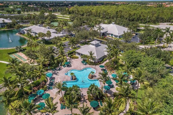 An aerial view of a resort with a central swimming pool, multiple buildings, and surrounding greenery.
