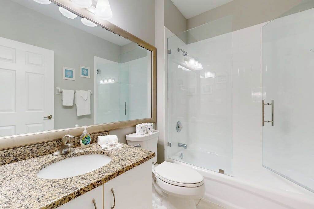 Une salle de bain dotée d’un lavabo avec un plan de toilette en granit, de toilettes, d’une douche à parois de verre et d’un grand miroir.