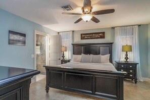 A bedroom with a dark wooden bed, a ceiling fan, a nightstand with a lamp, and a wall with a motivational quote. - Inviting home with saltwater pool, outdoor dining area, and internet (Naples)
