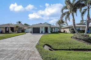 A residential property with a paved driveway, a garage, and a well-maintained lawn with palm trees. - Inviting home with saltwater pool, outdoor dining area, and internet (Naples)