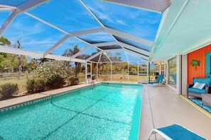 A swimming pool with a glass ceiling, surrounded by outdoor furniture and a view of the landscape. - Tropical paradise near the beach with enclosed private pool & lanai (Punta Gorda)