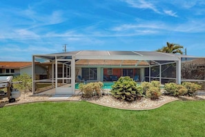 A covered outdoor area with a pool, surrounded by well-maintained grass and shrubs. - Tropical paradise near the beach with enclosed private pool & lanai (Punta Gorda)