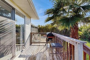 A wooden deck with a grill, a chair, and a palm tree. - Coastal Snowbird Retreat | 30+ Days (Port Charlotte)