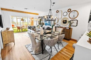 A modern dining area with a glass table, cushioned chairs, and a chandelier. - Stunning waterview condo w/ shared pool, hot tub, & private outdoor dining area (Naples)