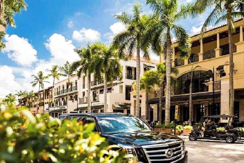 Ein Hotel mit mehreren Etagen, Palmen und einem schwarzen SUV, das an der Straße geparkt ist.