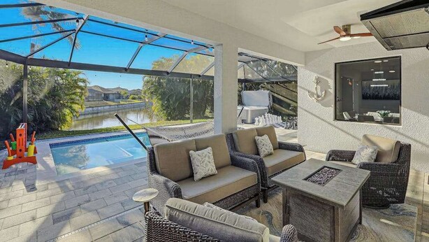 A poolside area with a sofa, chairs, and a table. - Canal front home with saltwater pool, hot tub, and washer and dryer. (Cape Coral)