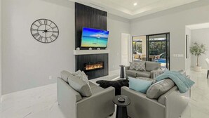 A modern living room with a fireplace, a mounted TV, and a ceiling fan. - Canal front home with saltwater pool, hot tub, and washer and dryer. (Cape Coral)